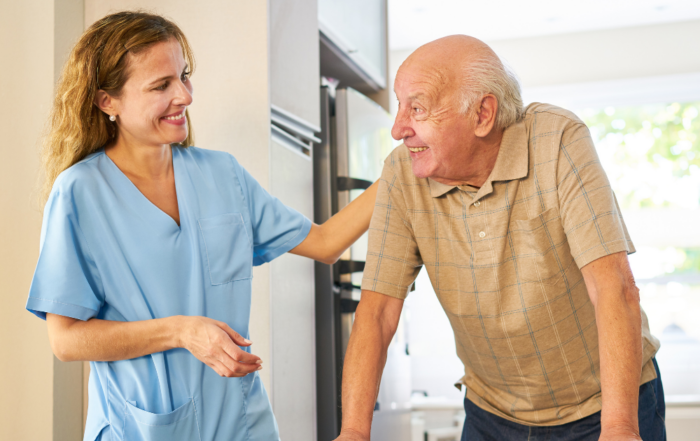 Caregiver smiling at senior man using a walker while providing ambulation assistance, a senior home care service.